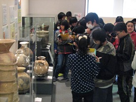 亀山で出土した縄文土器や弥生土器の前でメモを取る児童たち